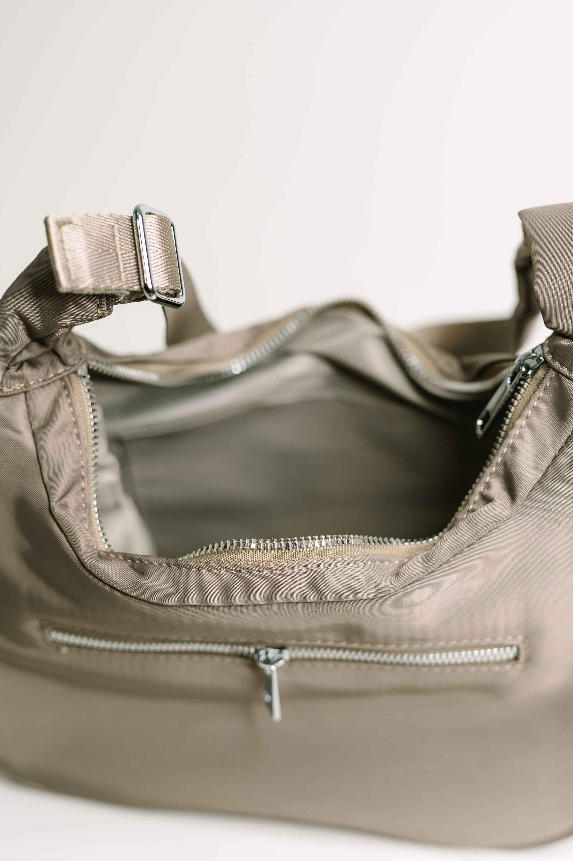 Close-up of a beige handbag with zippers on a light background
