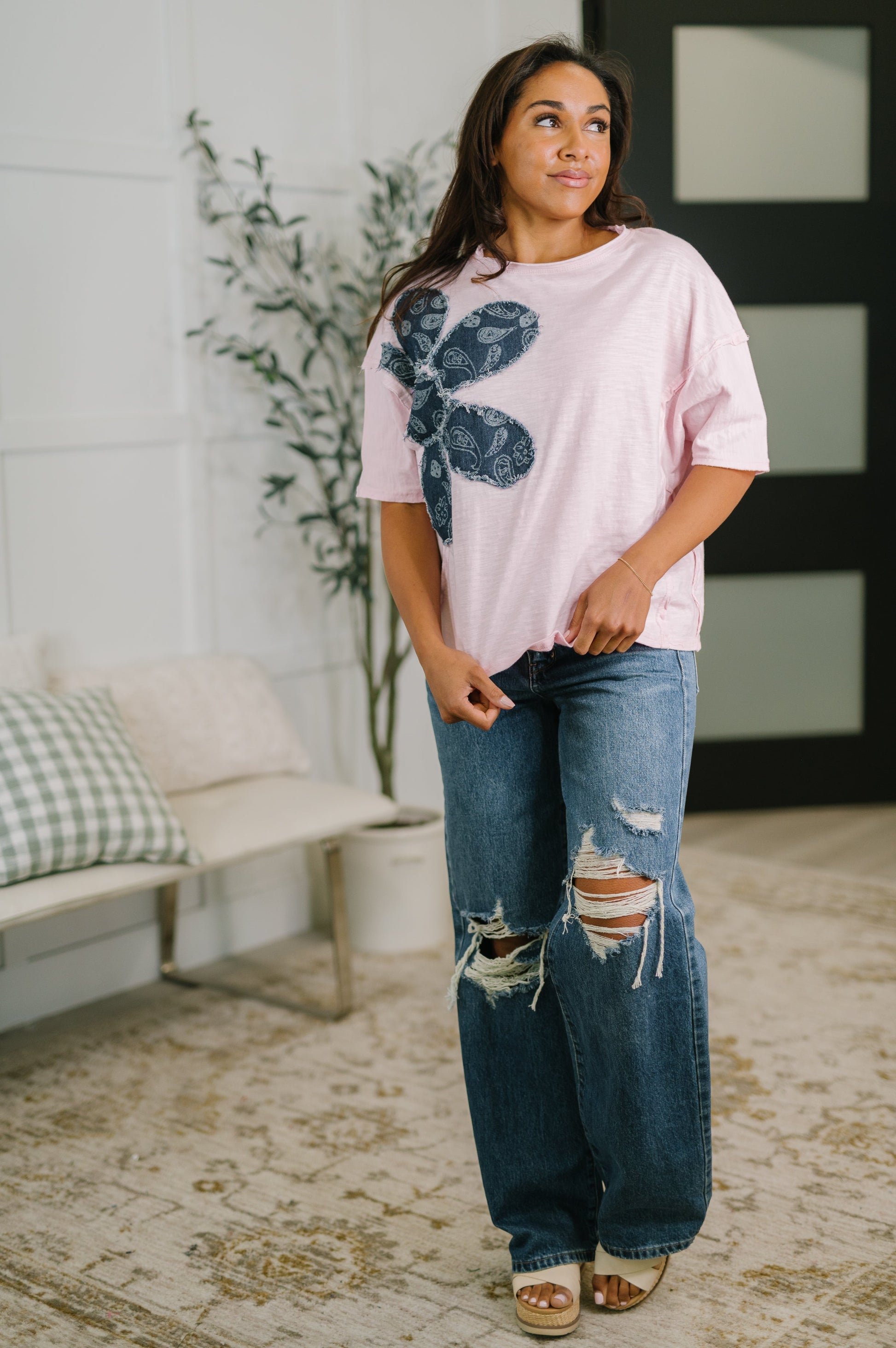 Woman wearing a pink oversized shirt with a floral design and ripped jeans in a living room.