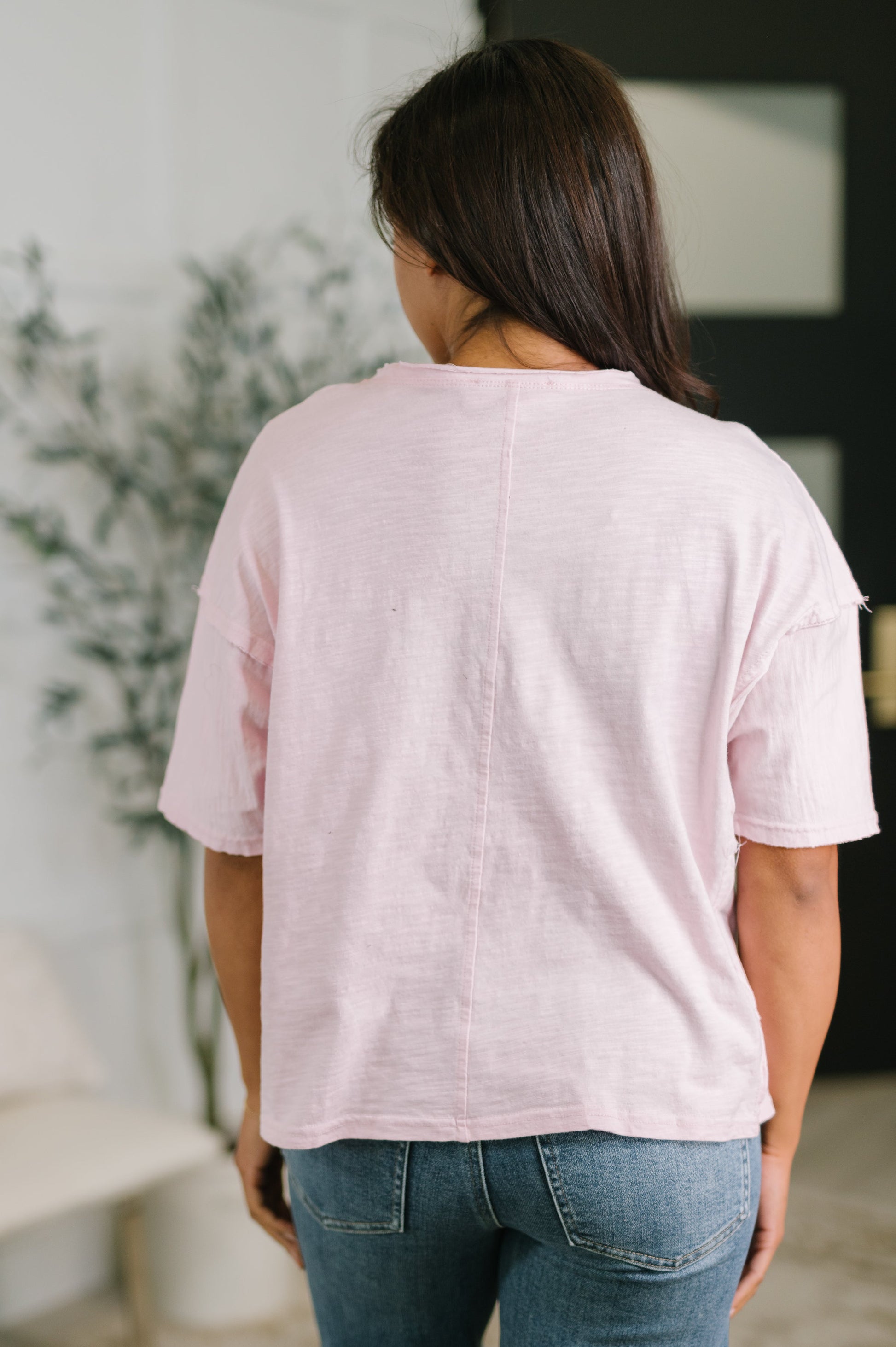 Person wearing a light pink t-shirt and blue jeans in an indoor setting