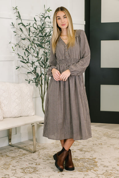 Woman wearing a plaid dress standing in a room with a plant and a bench.