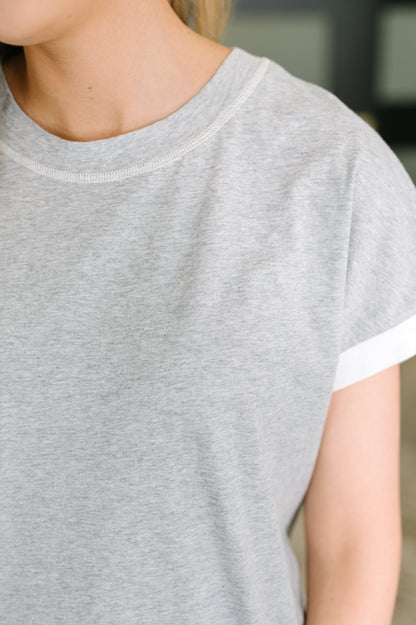 Close-up of a person wearing a light heather gray short-sleeve t-shirt with a white contrast trim along the sleeve cuff.