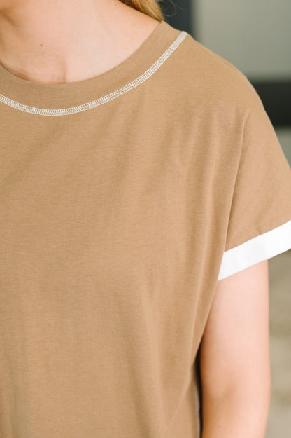 Close-up of a person wearing a tan short-sleeve top with white contrast trim along the neckline and sleeve cuffs.
