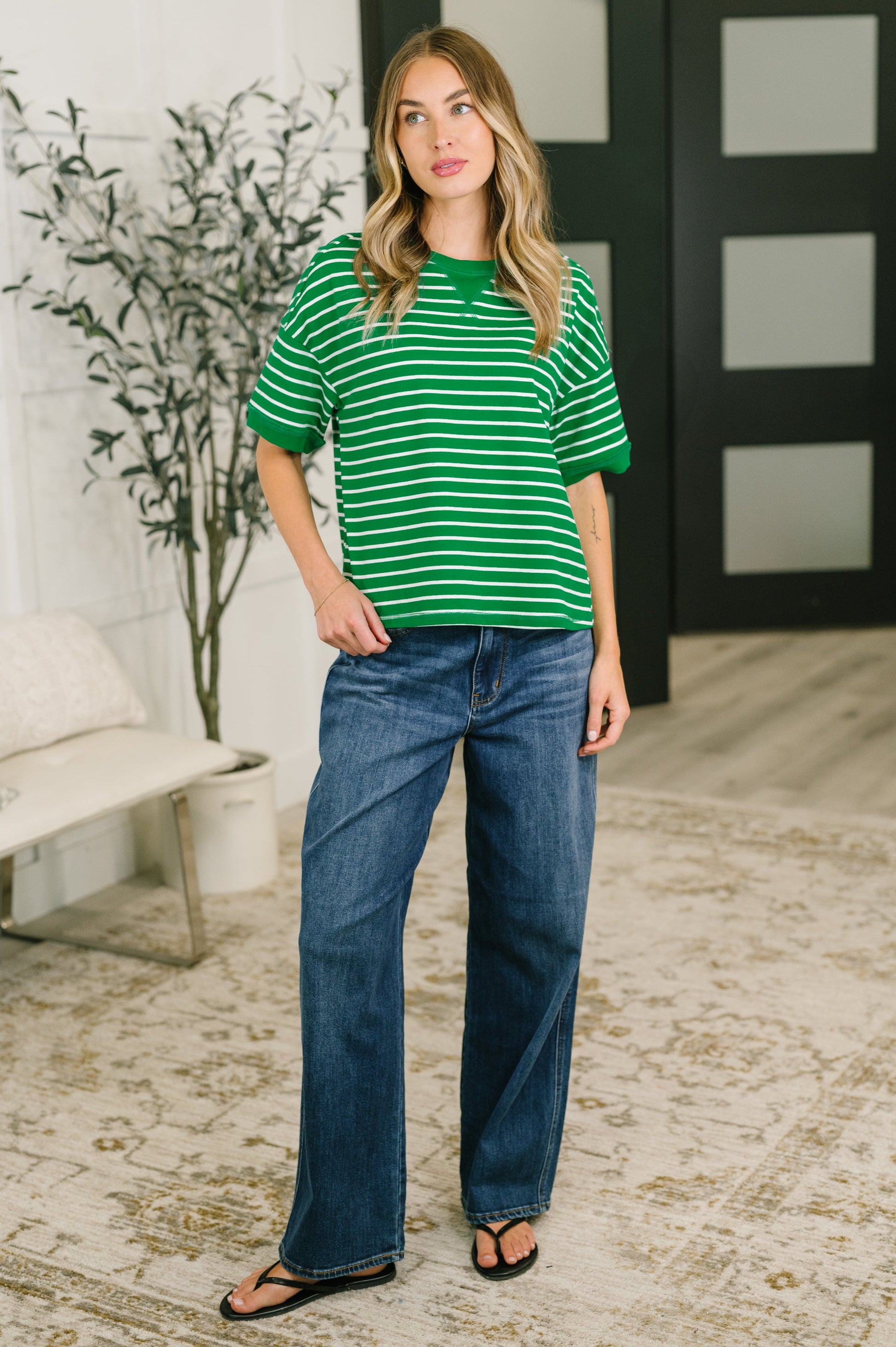 Woman wearing a green and white striped shirt and blue jeans indoors.