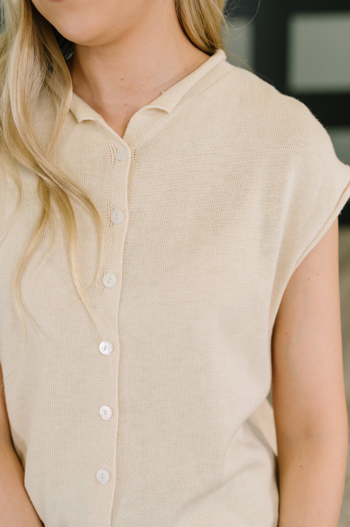 Close-up of a woman wearing a light beige short-sleeve knit top with a buttoned collar and front buttons.