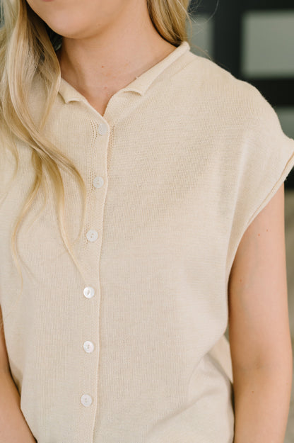 Close-up of a woman wearing a light beige short-sleeve knit top with a buttoned collar and front buttons.