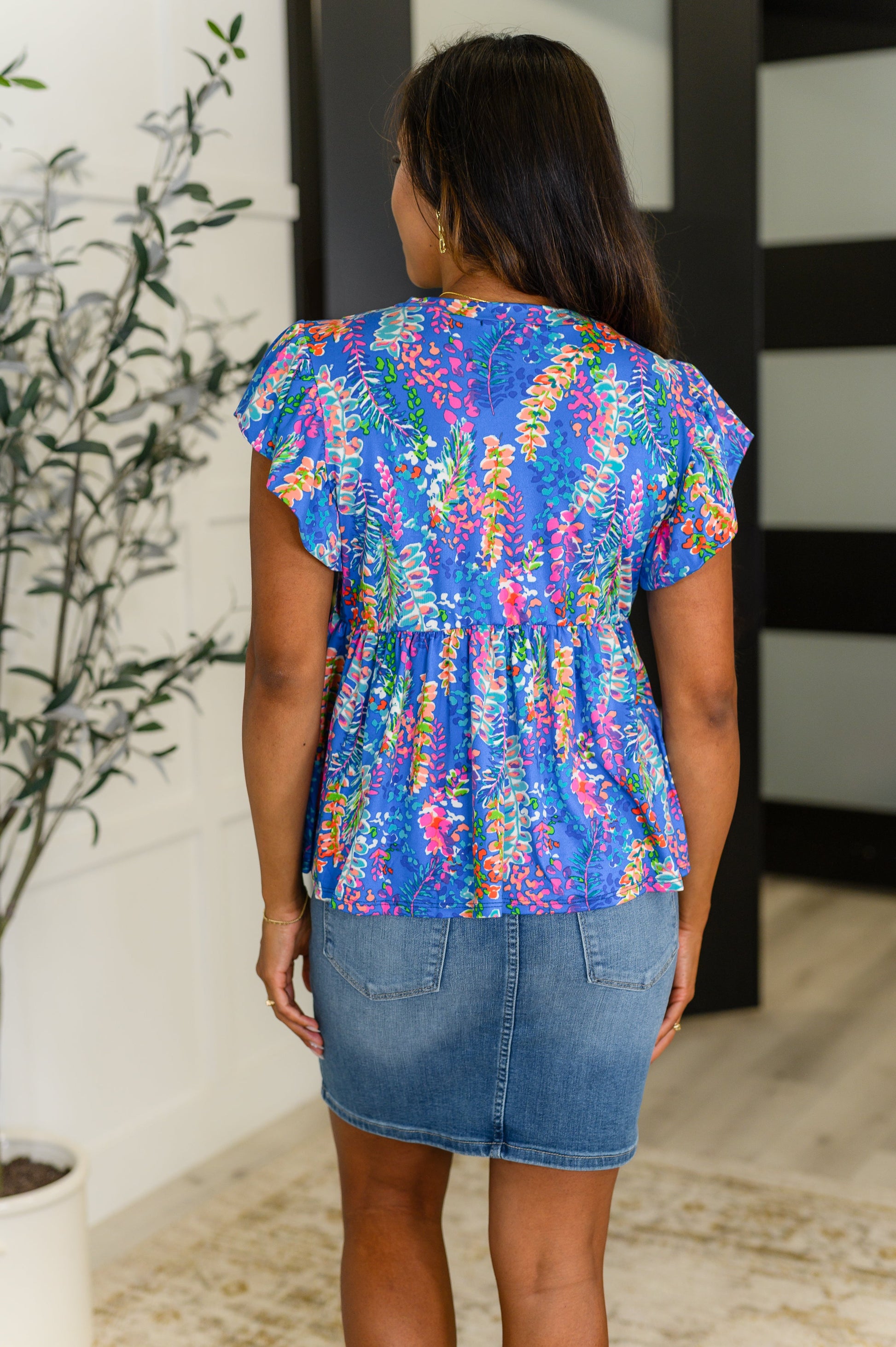 Woman wearing a colorful floral blouse and denim skirt in an indoor setting.