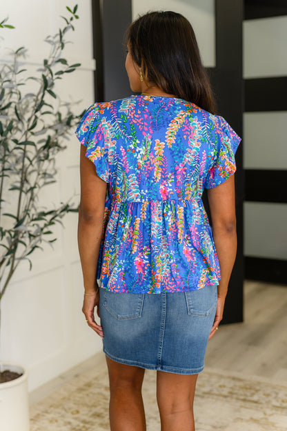 Woman wearing a colorful floral blouse and denim skirt in an indoor setting.