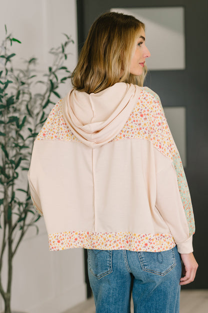 Woman wearing a light pink hoodie with floral patterns and blue jeans indoors.