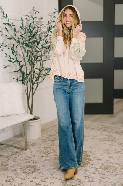 Woman wearing a beige hoodie and blue jeans standing in a living room.