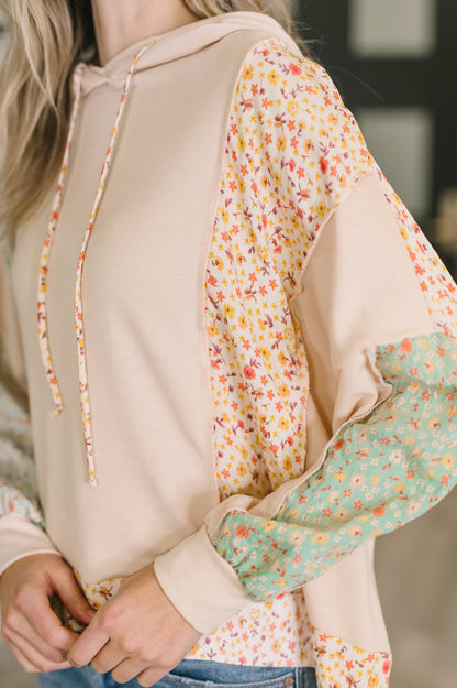 Close-up of a person wearing a beige hoodie with floral patterned sleeves.