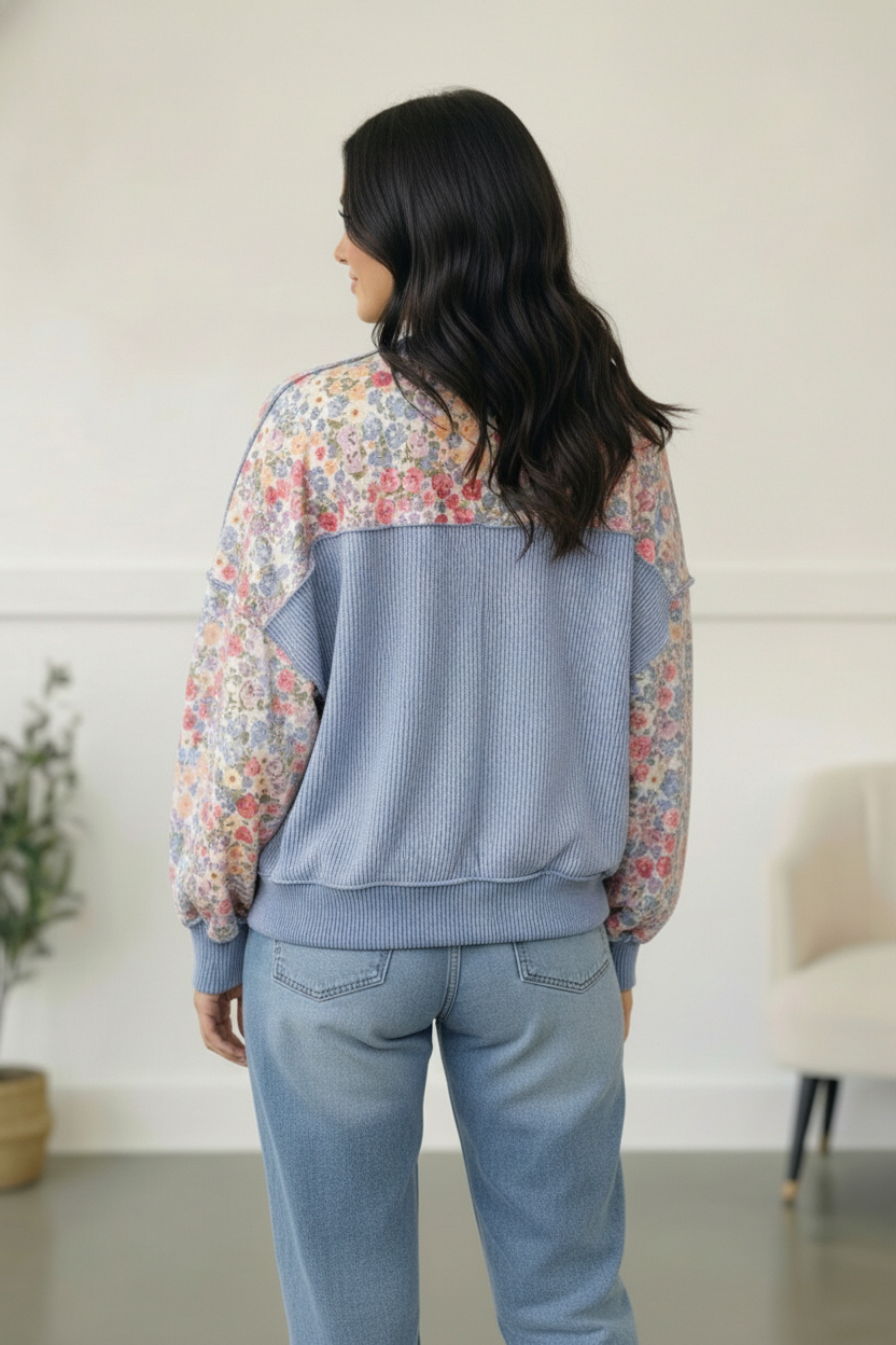 Woman wearing a floral long-sleeve top and light blue jeans indoors.