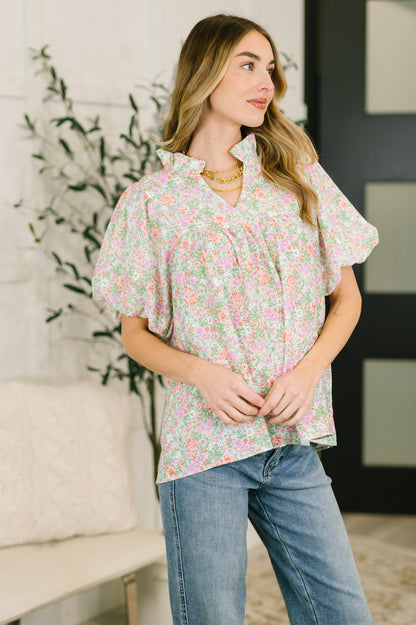 Woman wearing a floral blouse and jeans standing in a room with a plant and furniture.