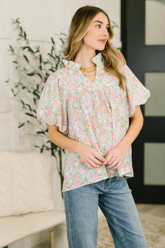 Woman wearing a floral blouse and jeans standing in a room with a plant and furniture.