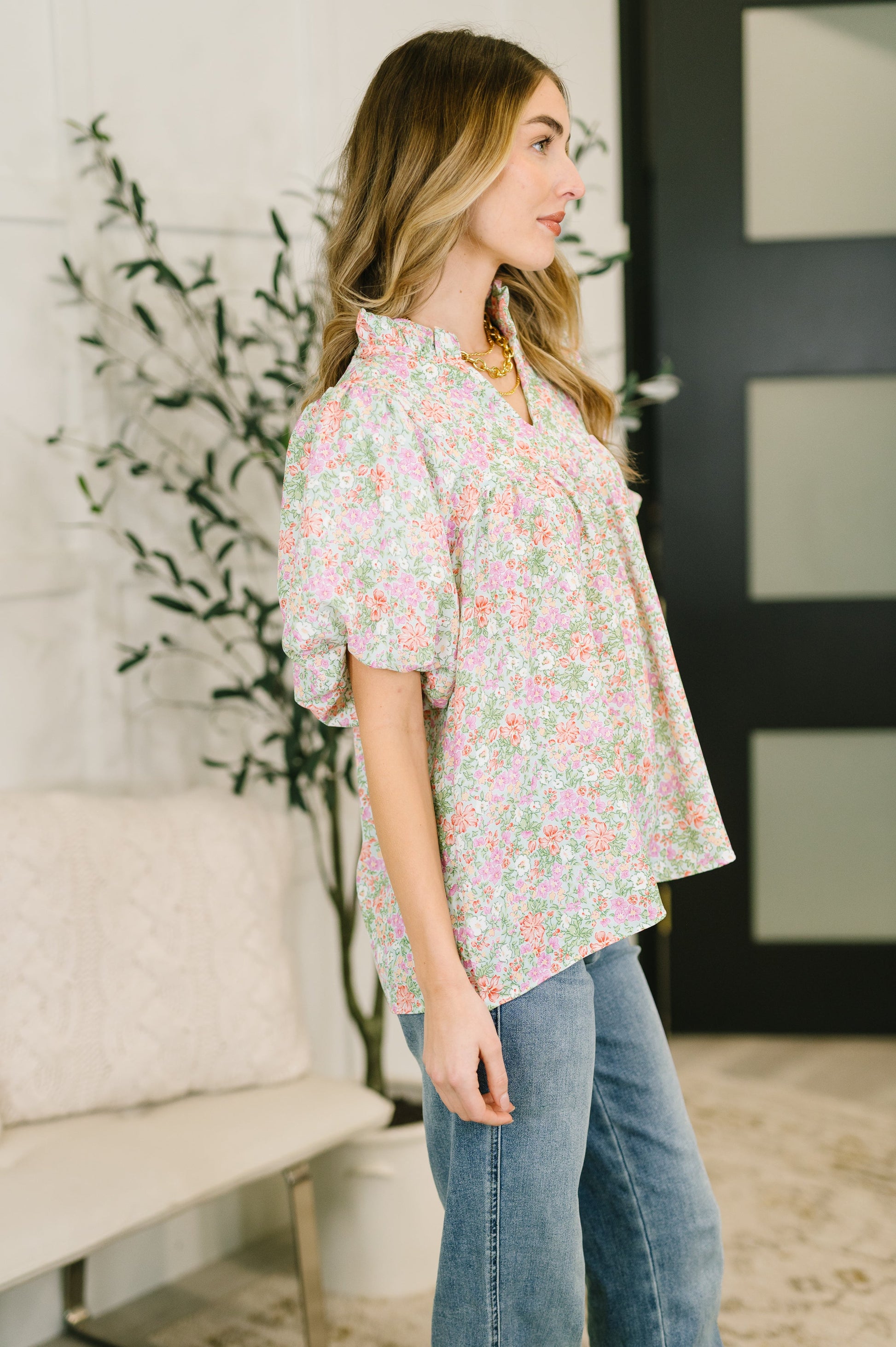 Woman wearing a floral blouse and jeans in a room with a plant and door.