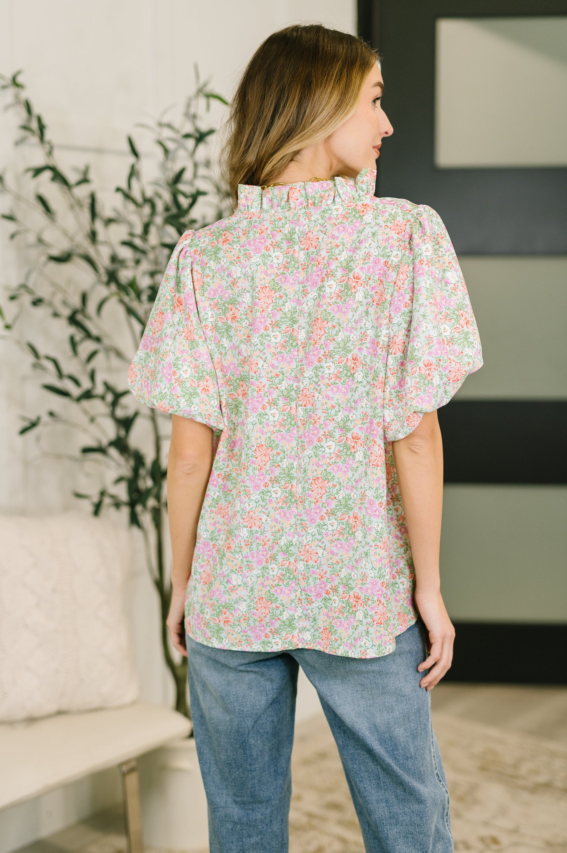 Woman wearing a floral blouse and jeans in a room with a plant and couch.