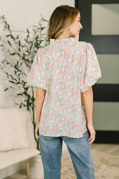 Woman wearing a floral blouse and jeans in a room with a plant and couch.