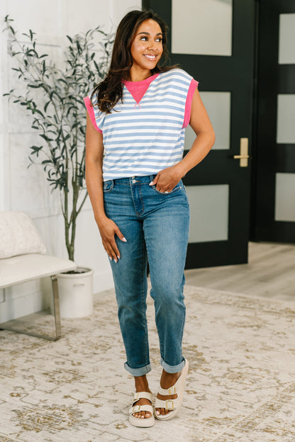 Woman wearing a striped shirt and jeans standing in a room with a plant and door in the background.