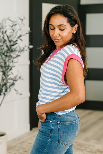 Woman wearing a striped shirt with pink trim and blue jeans, standing outdoors.