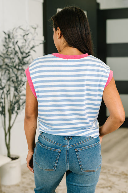 Person wearing a blue and pink striped sleeveless top with jeans, standing in an indoor setting.