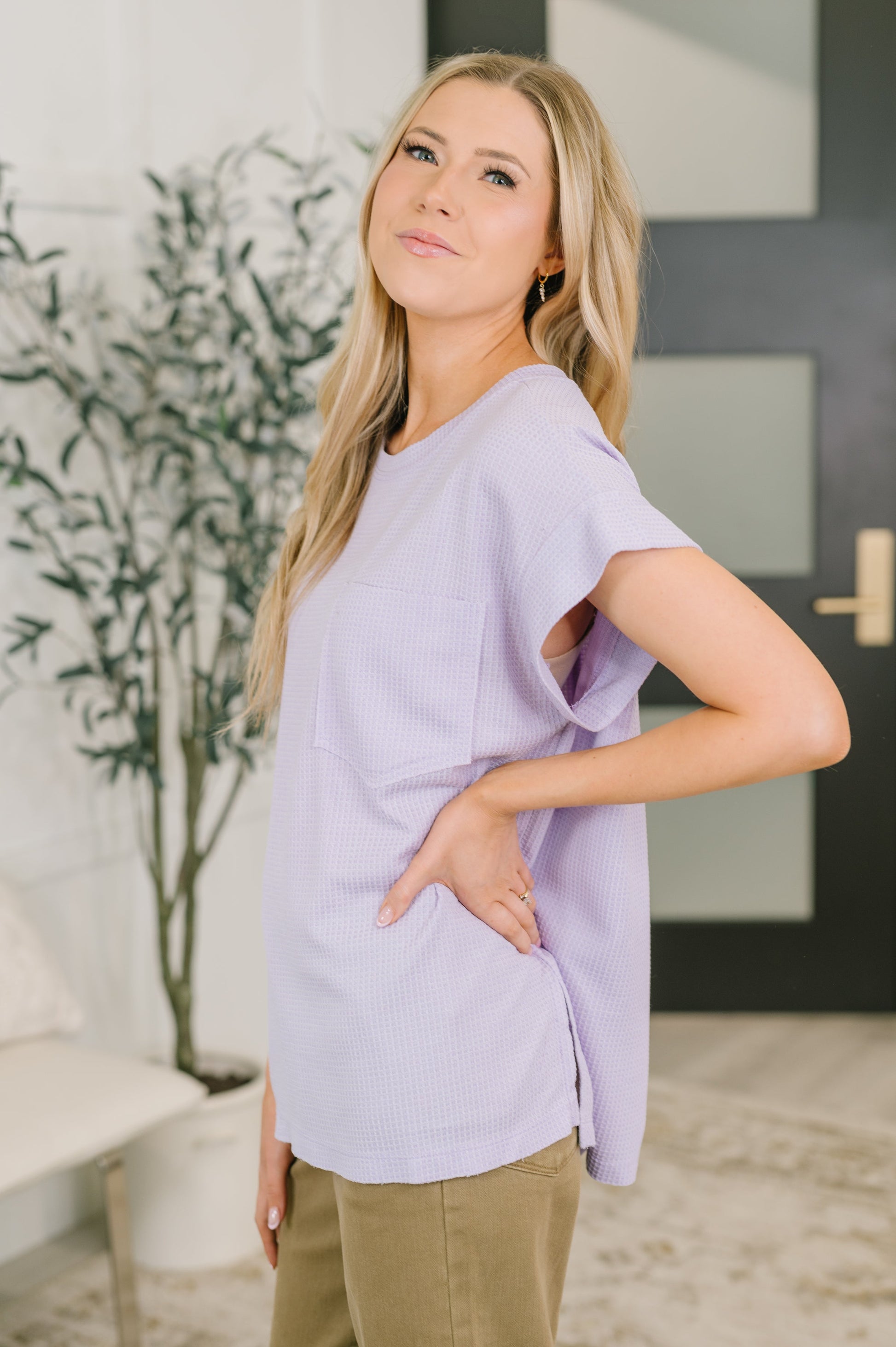 Woman wearing a light purple t-shirt indoors with a plant and door in the background