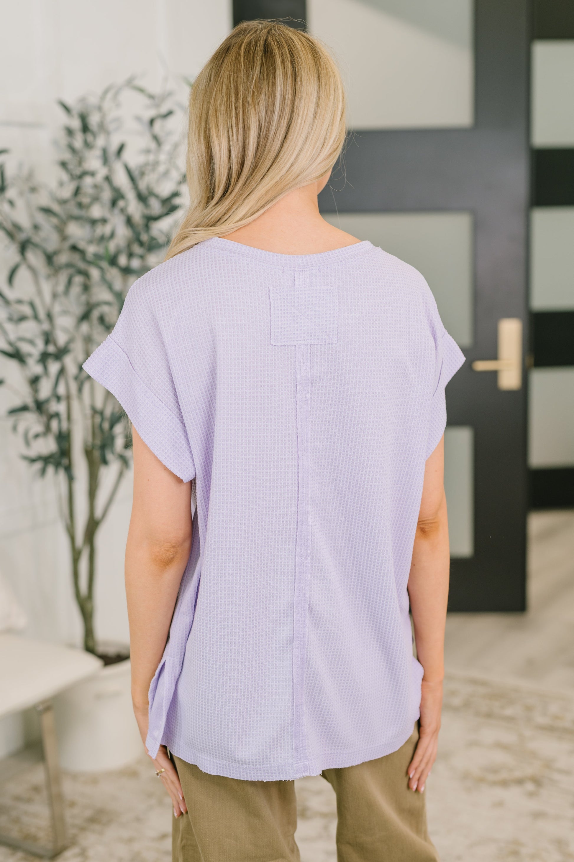 Person wearing a light purple top standing in front of a door.