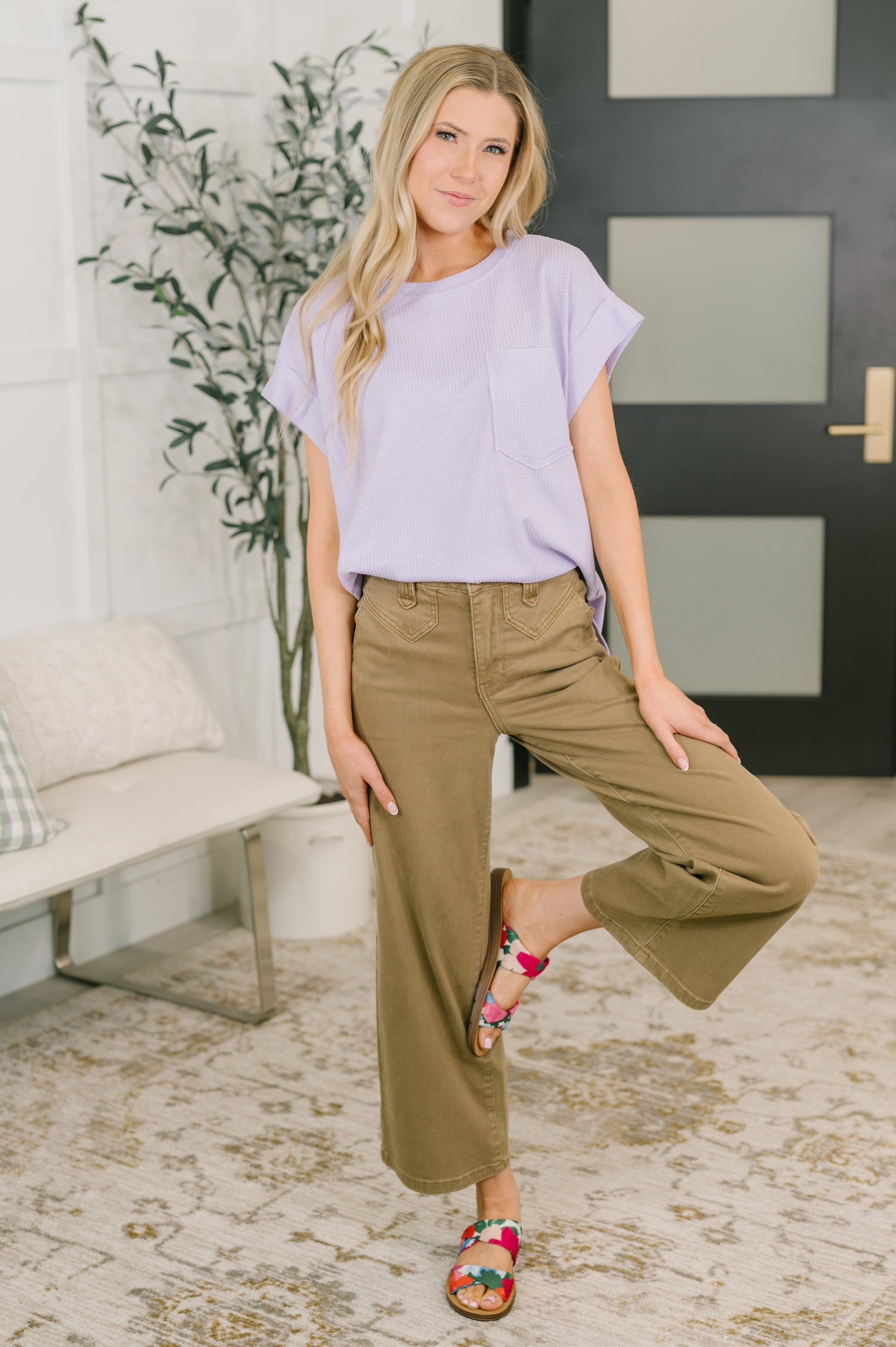 Woman wearing a light purple top and beige pants in an indoor setting.