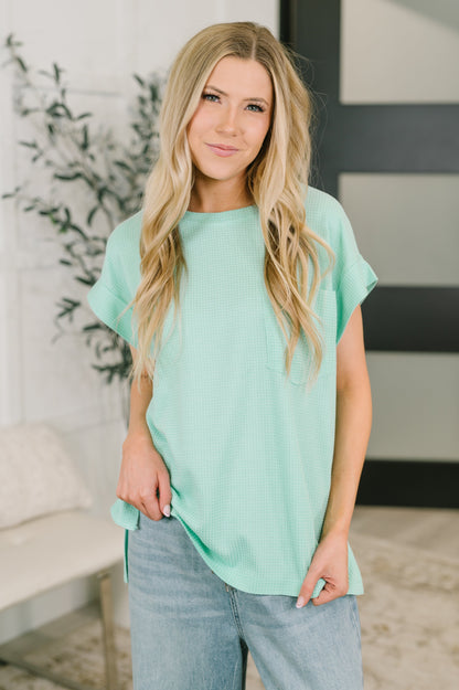 Woman wearing a light green top and blue jeans indoors.