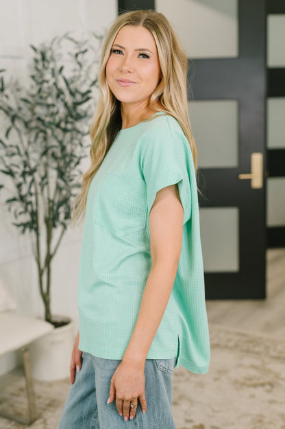 Woman wearing a light green top in an indoor setting with a plant and door in the background