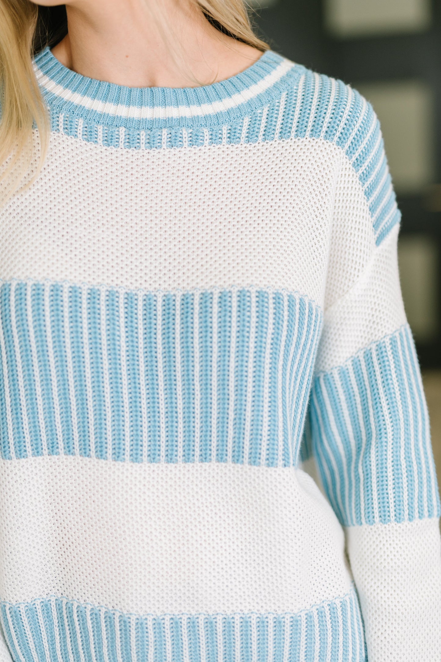 Close-up of a person wearing a white sweater with blue stripes.