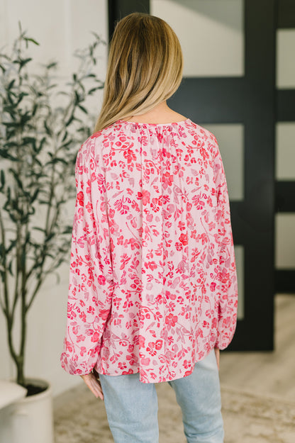 Person wearing a pink floral blouse with a blurred background
