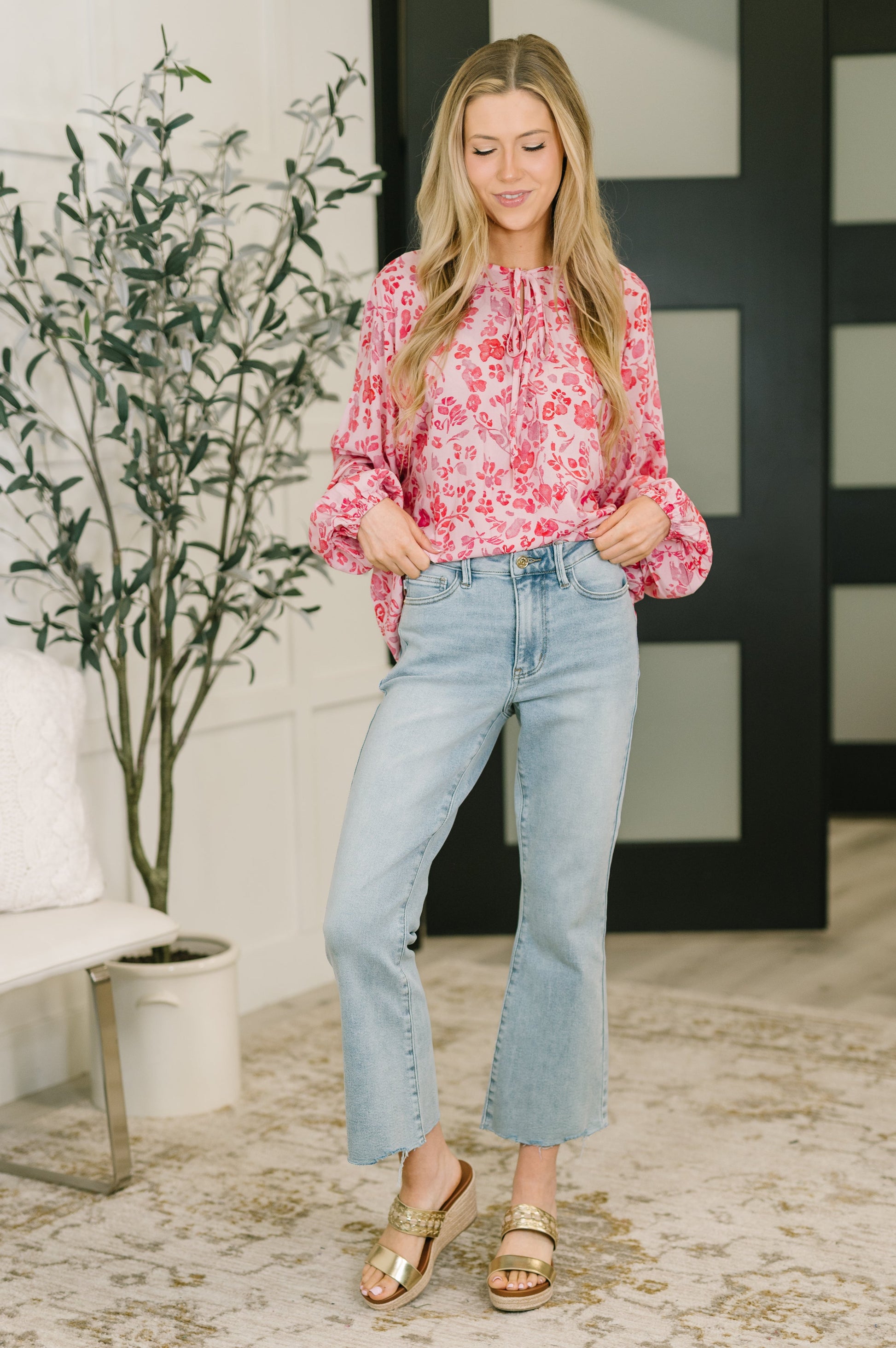 Woman wearing a pink floral blouse and light blue jeans standing indoors.