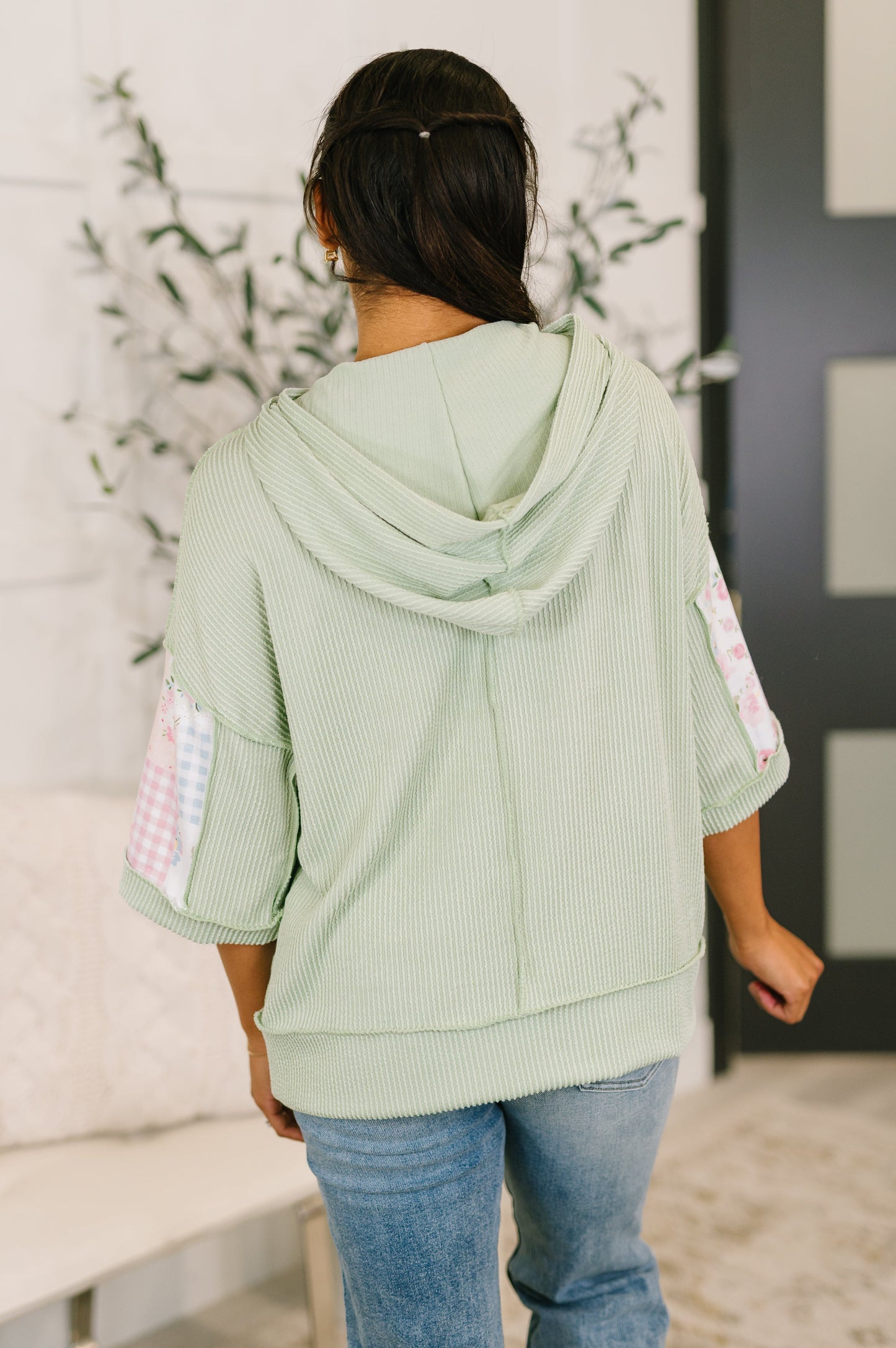 Person wearing a light green hoodie with checkered sleeves in an indoor setting