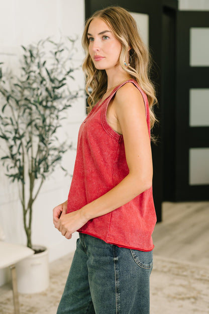 Woman wearing a red tank top and blue jeans standing outdoors.