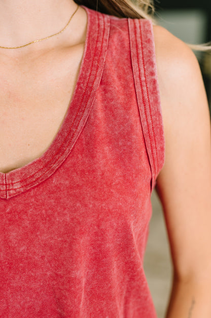 Close-up of a person wearing a washed red racerback tank top, showing the shoulder, chest, and neckline against a softly blurred background.