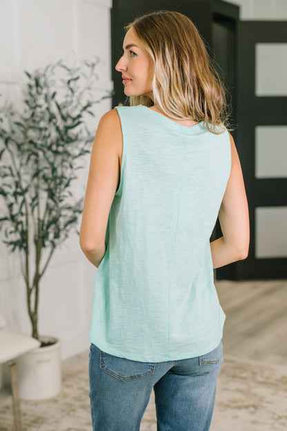 Woman wearing a light blue sleeveless top and jeans in an indoor setting.