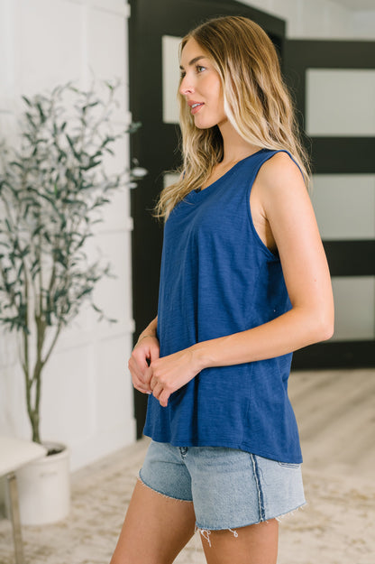 Woman wearing a blue sleeveless top and denim shorts standing indoors.