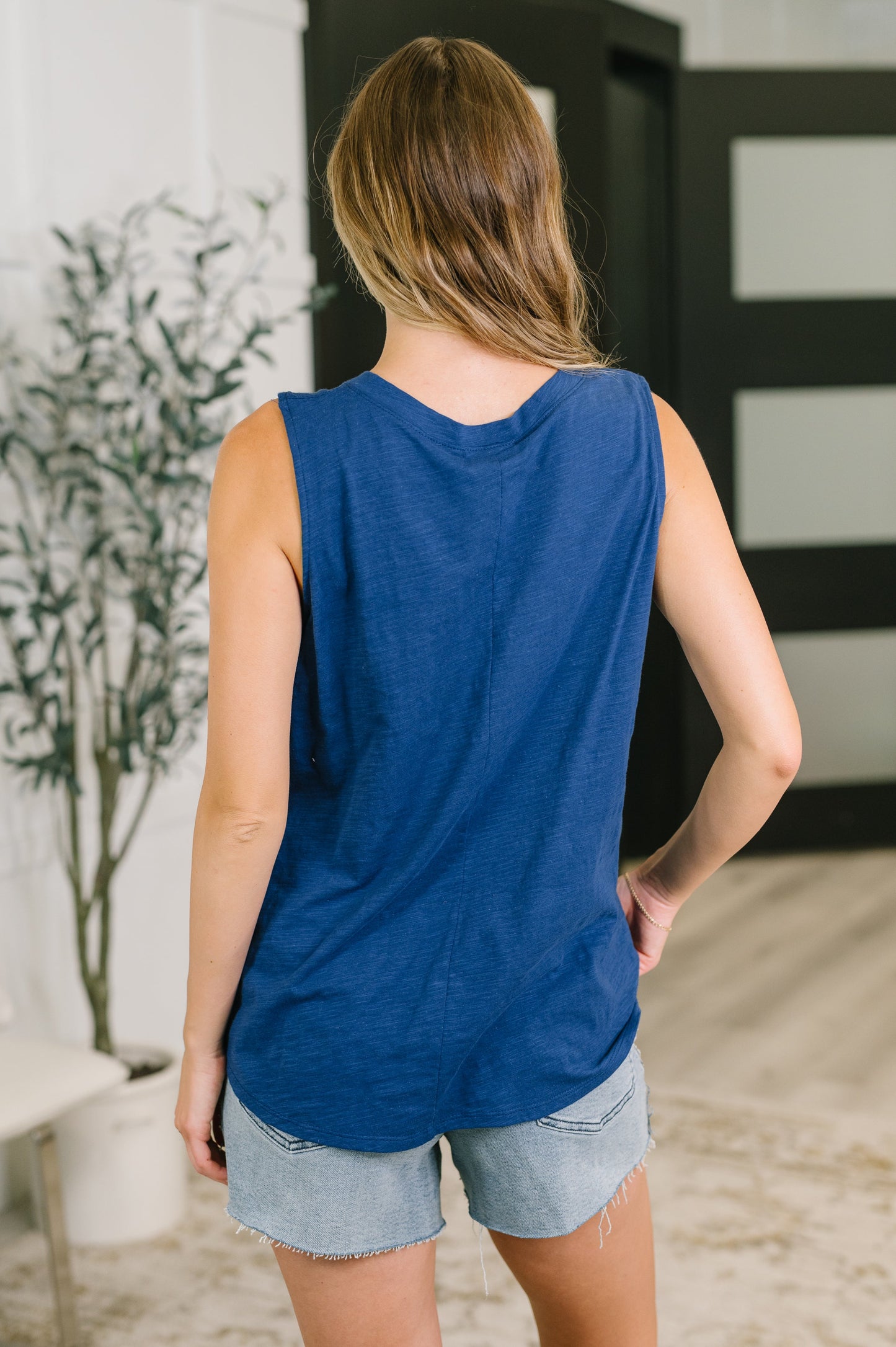 Woman wearing a blue sleeveless top and denim shorts in an indoor setting.