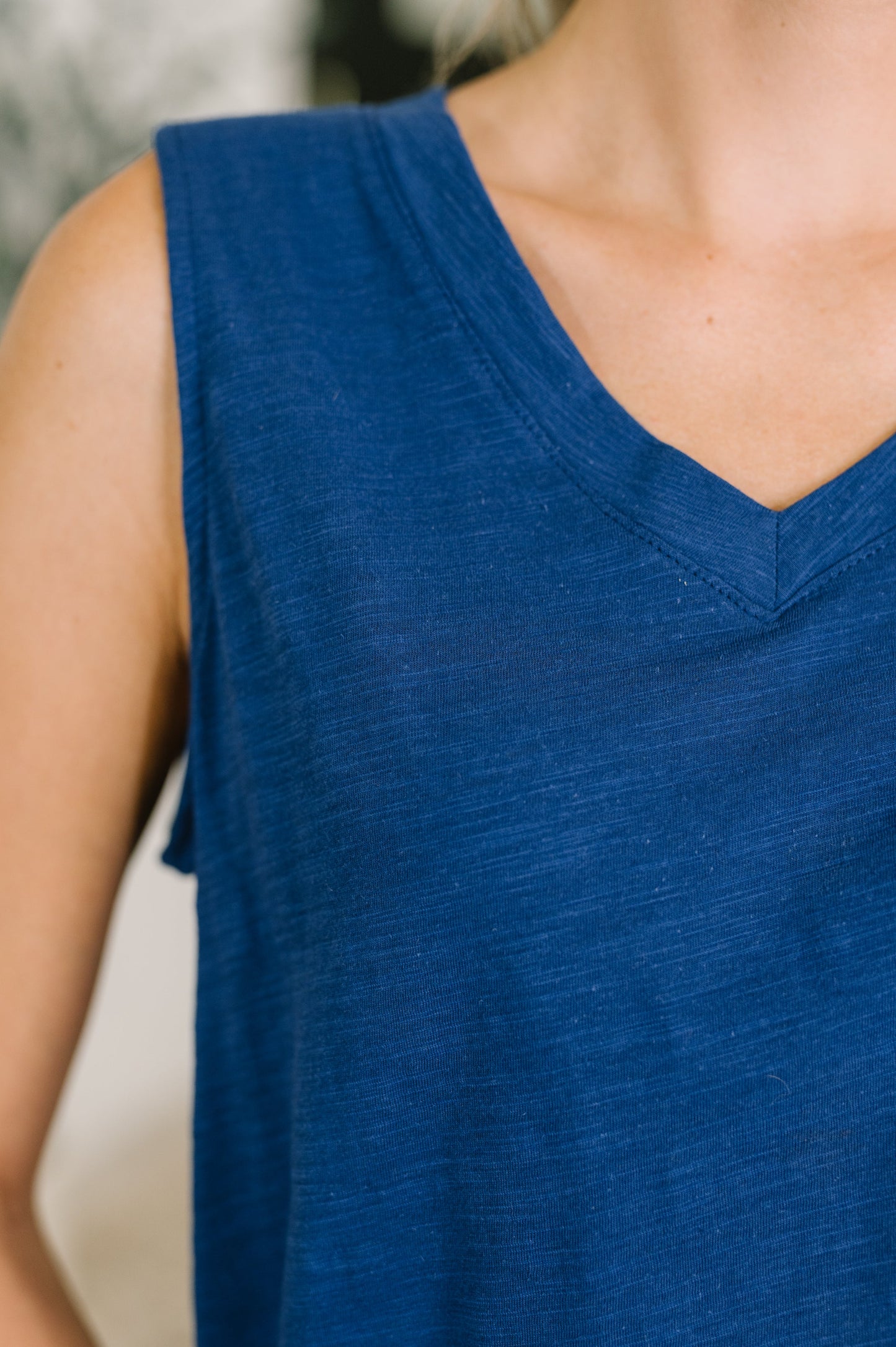 Close-up of a person wearing a blue sleeveless top with a blurred background
