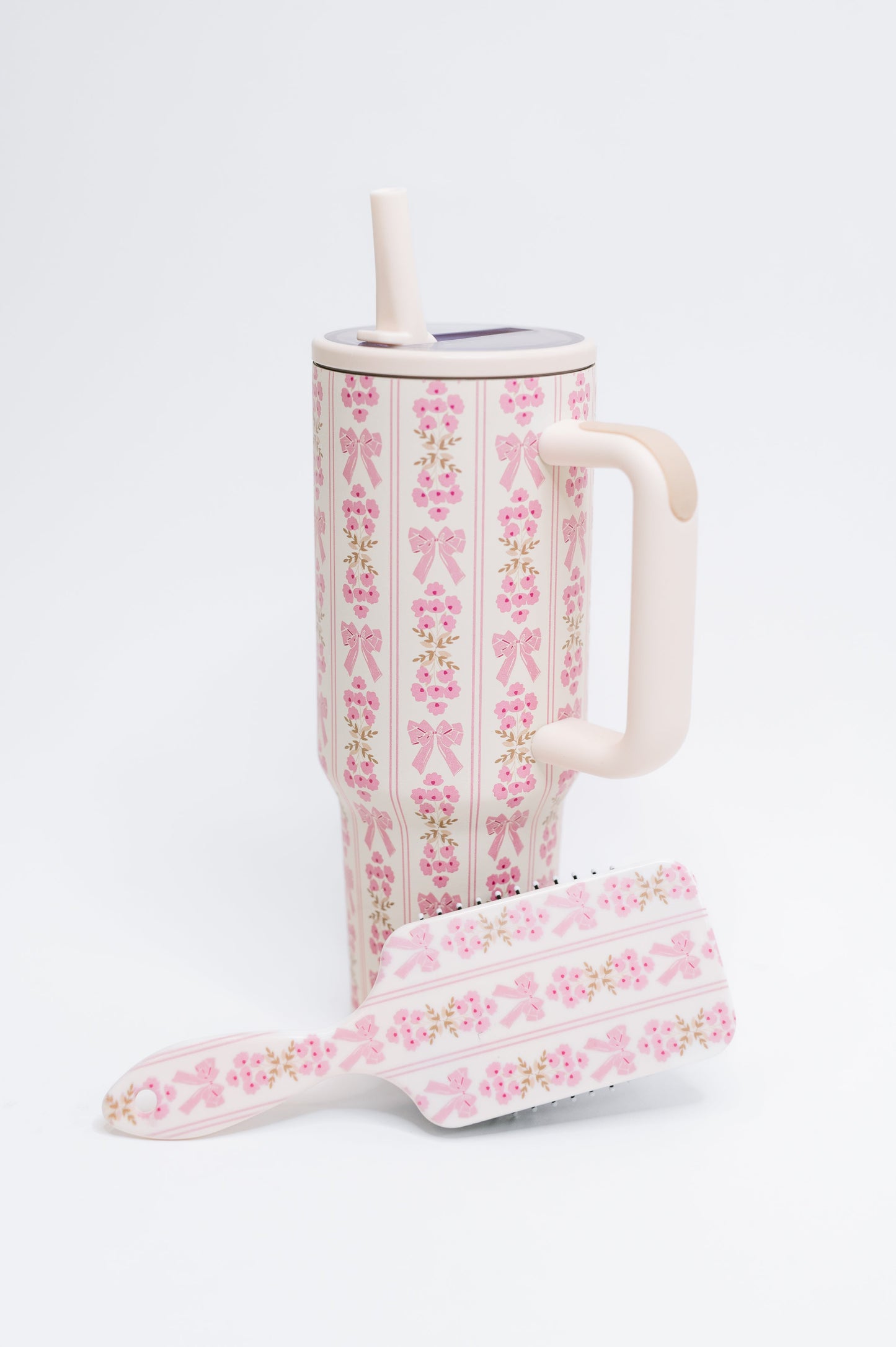 Floral-patterned tumbler with straw and matching hairbrush on a white background