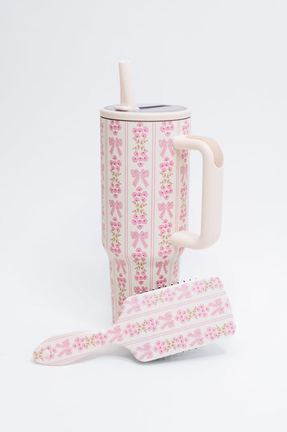 Floral-patterned tumbler with straw and matching hairbrush on a white background
