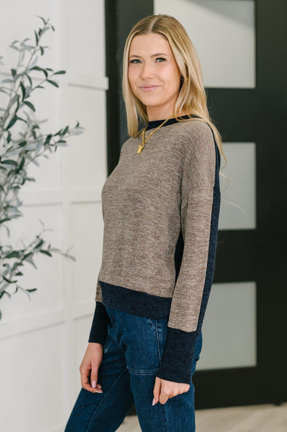 Woman wearing a two-tone sweater and jeans standing indoors with a plant in the background
