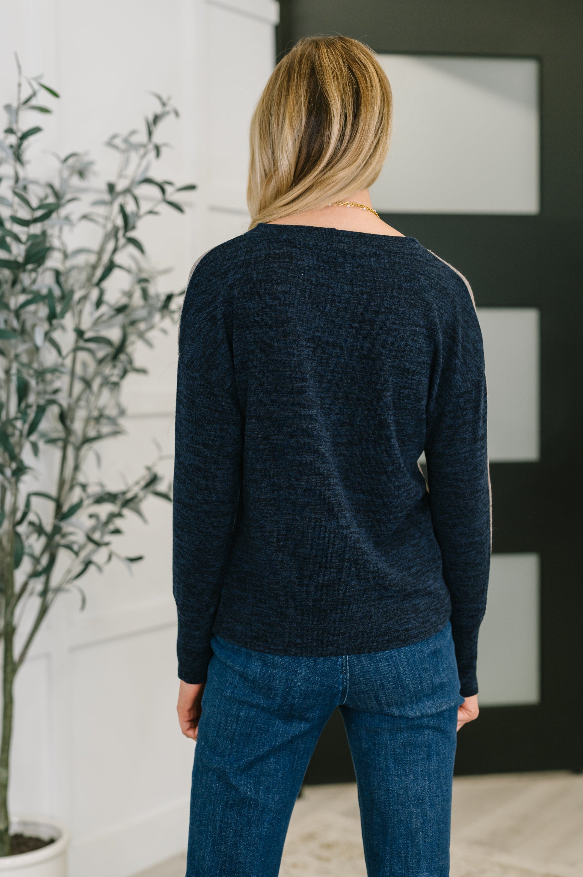 Person wearing a dark blue sweater and jeans standing in a room with a plant and a black and white abstract painting.
