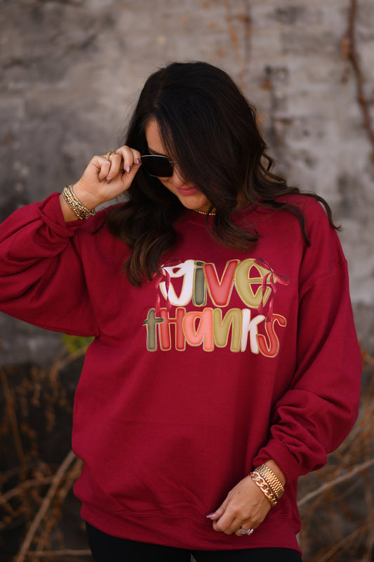 Person wearing a red sweatshirt with 'Give Thanks' text against a stone wall.