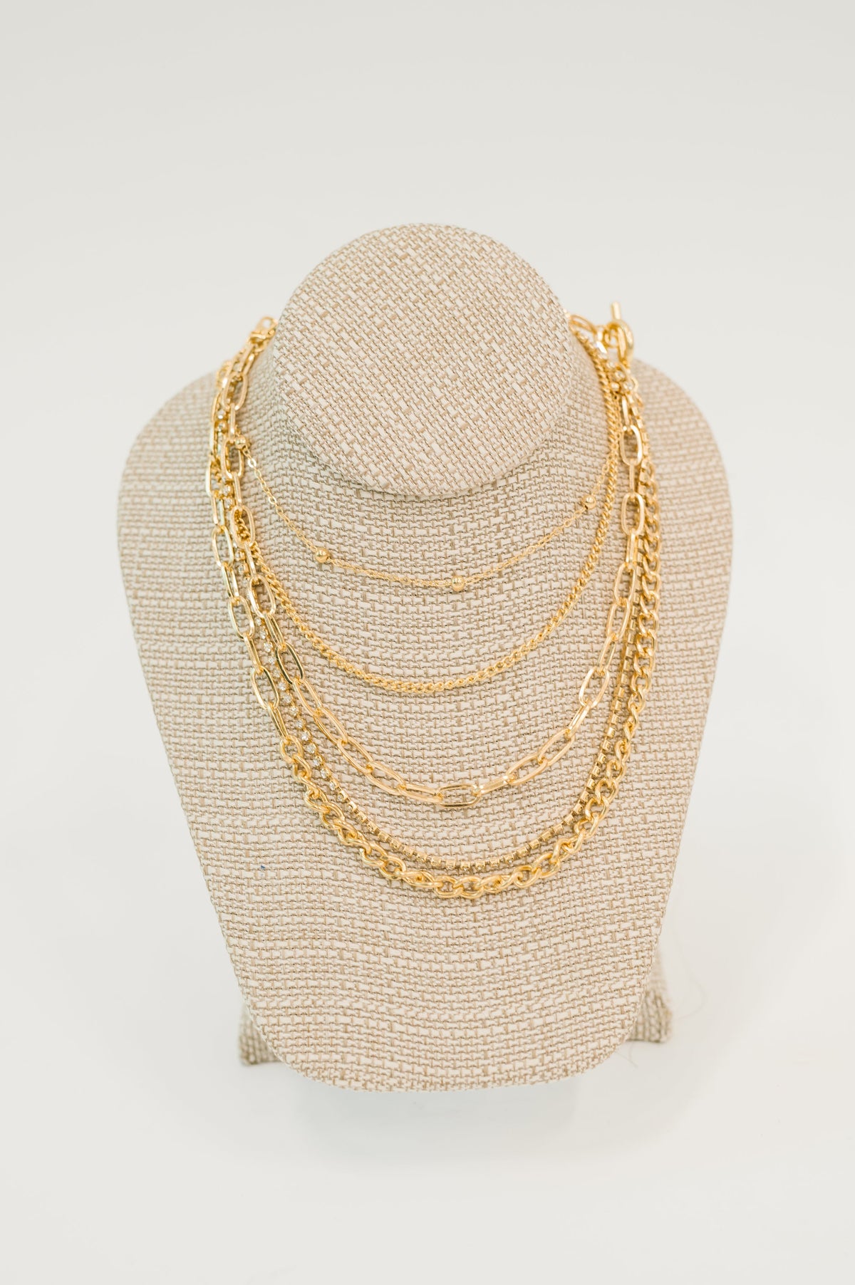 Gold chain necklace on a beige mannequin bust against a white background