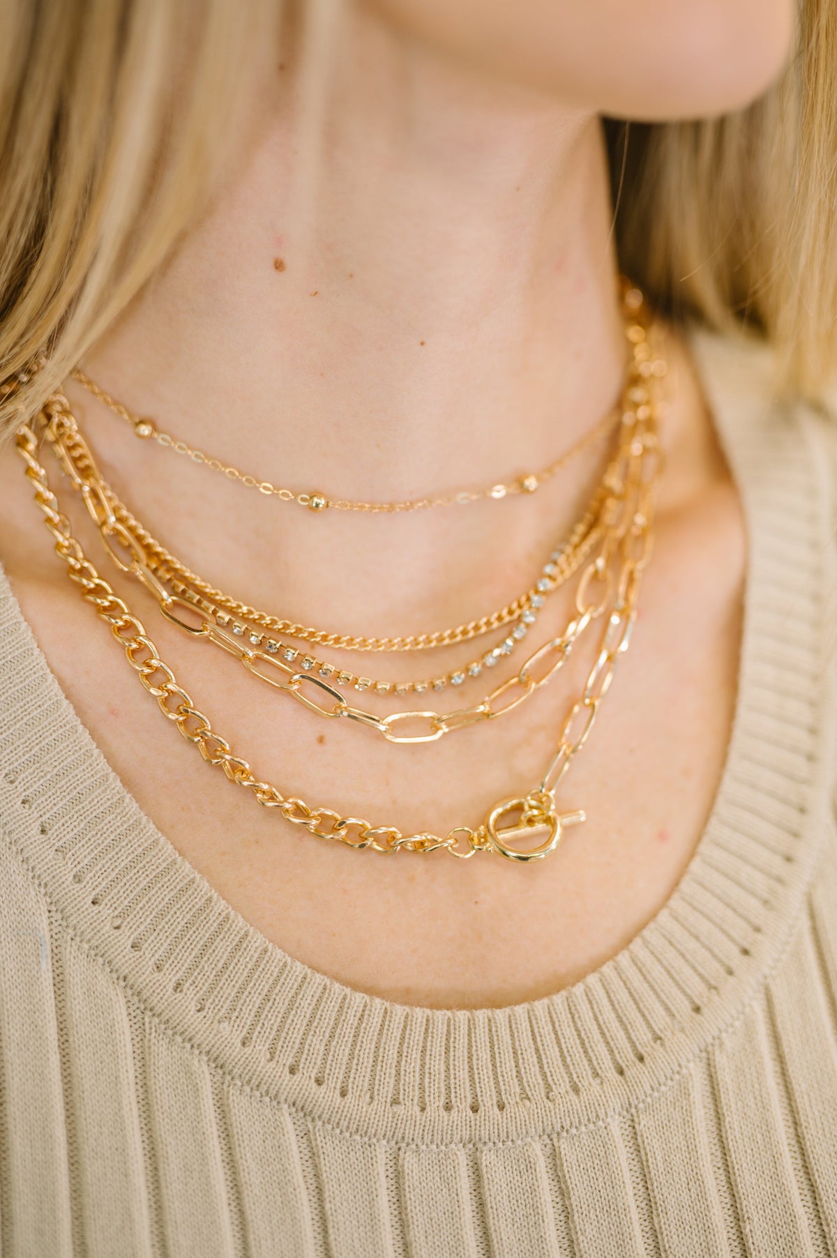 Close-up of a person wearing multiple gold necklaces on a beige sweater.