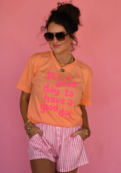 Woman wearing an orange t-shirt with pink text and pink shorts against a pink background