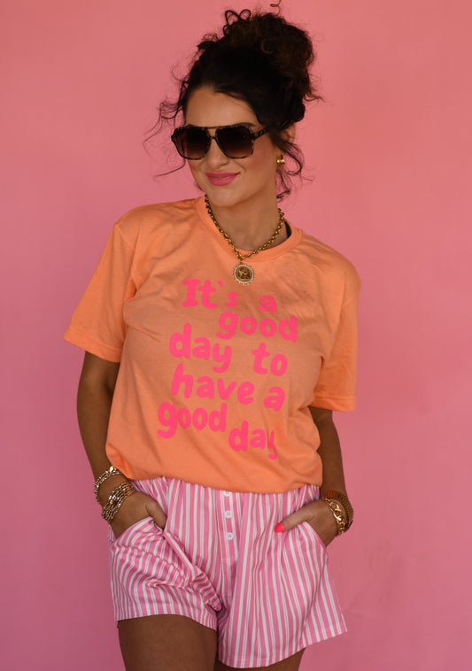 Woman wearing an orange t-shirt with pink text and pink shorts against a pink background