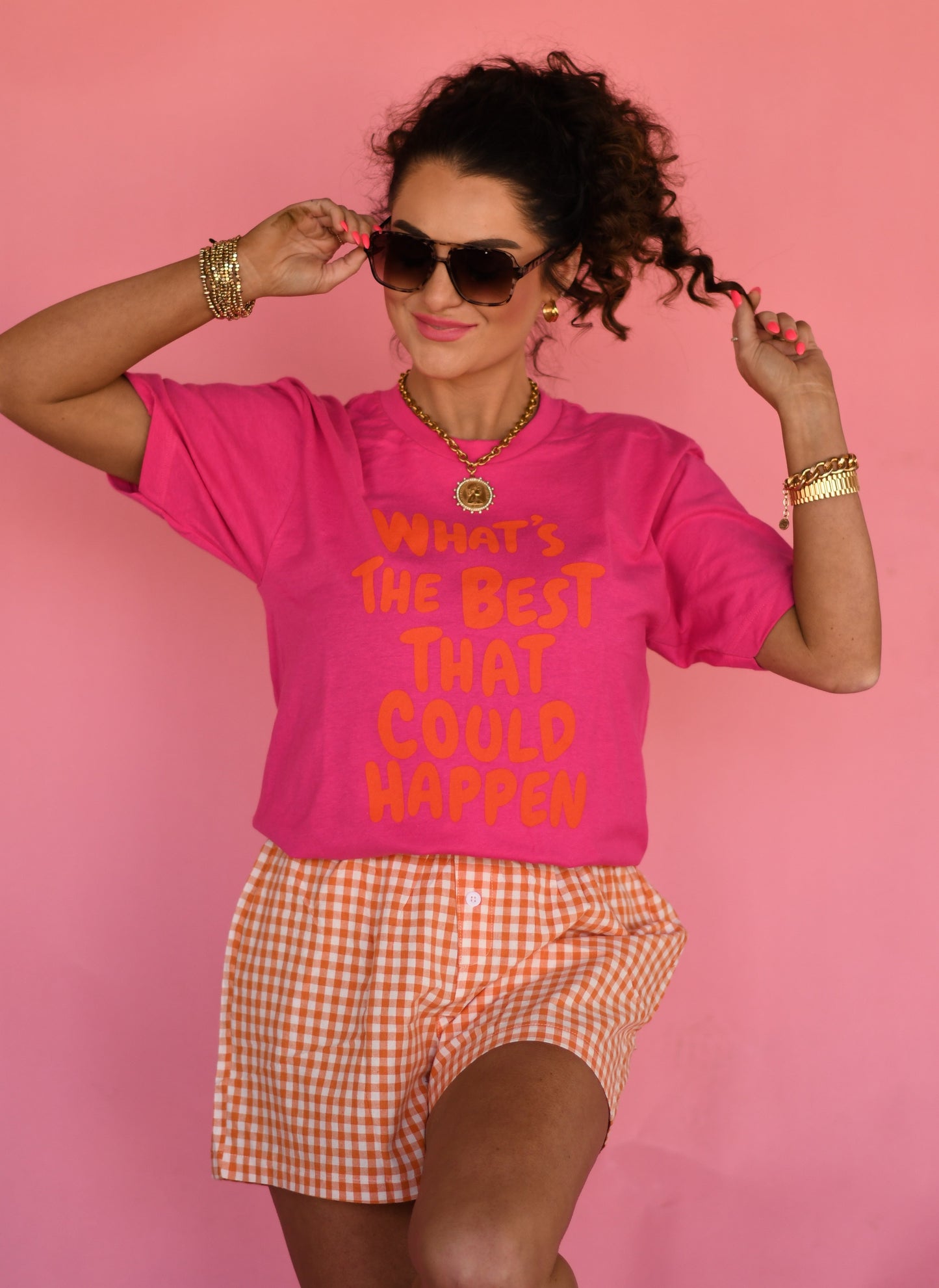 Woman wearing a pink t-shirt with text and orange checkered shorts on a pink background