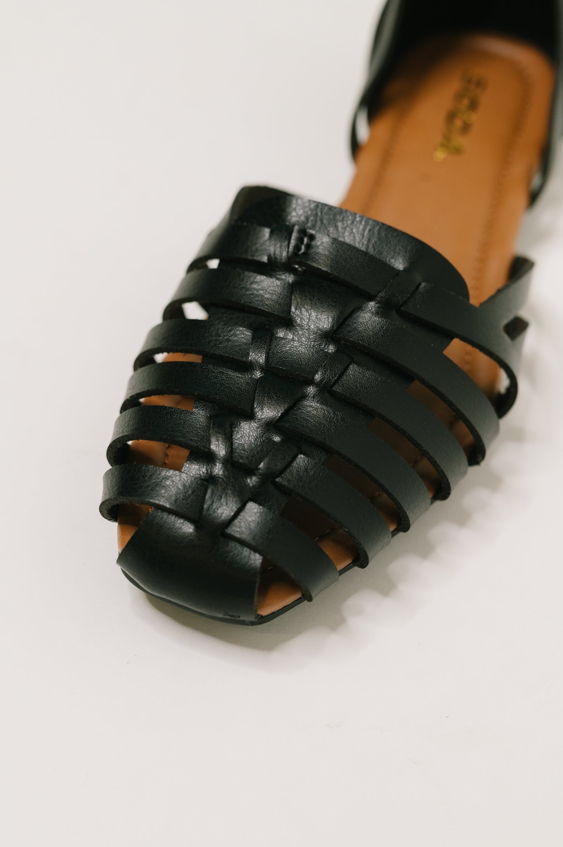 Black sandal with woven straps on a light gray background