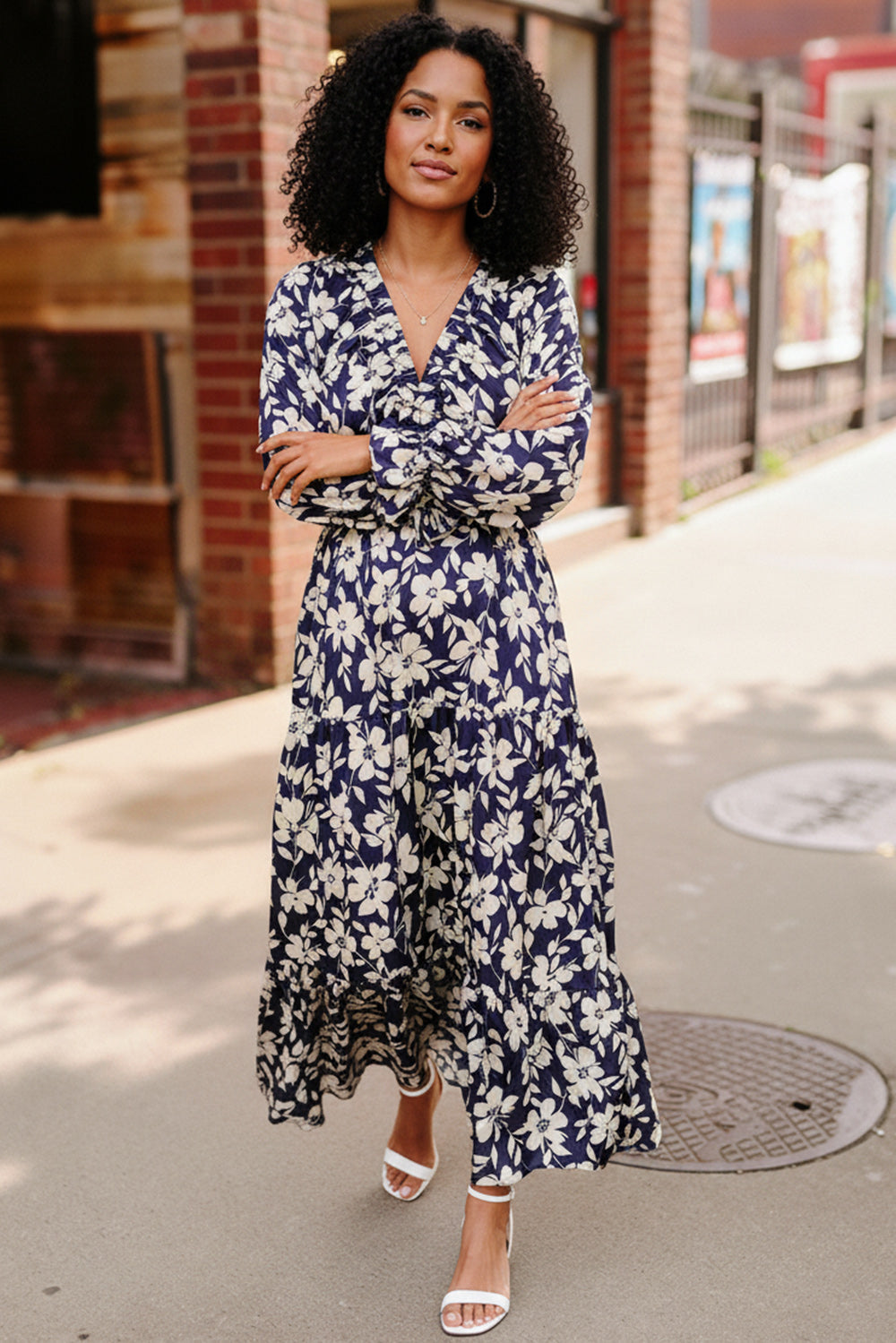 Woman wearing a blue floral dress standing on a sidewalk.